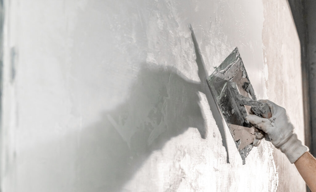 Close-up of a worker using a metal trowel to apply a smooth layer of moisture-resistant plaster to an interior wall, showcasing advanced damp proofing techniques for high-humidity environments.