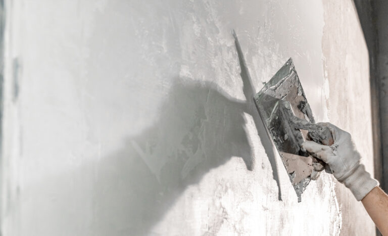 Close-up of a worker using a metal trowel to apply a smooth layer of moisture-resistant plaster to an interior wall, showcasing advanced damp proofing techniques for high-humidity environments.