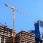 A high-rise building under development by construction companies in London featuring a large yellow tower crane against a clear blue sky.
