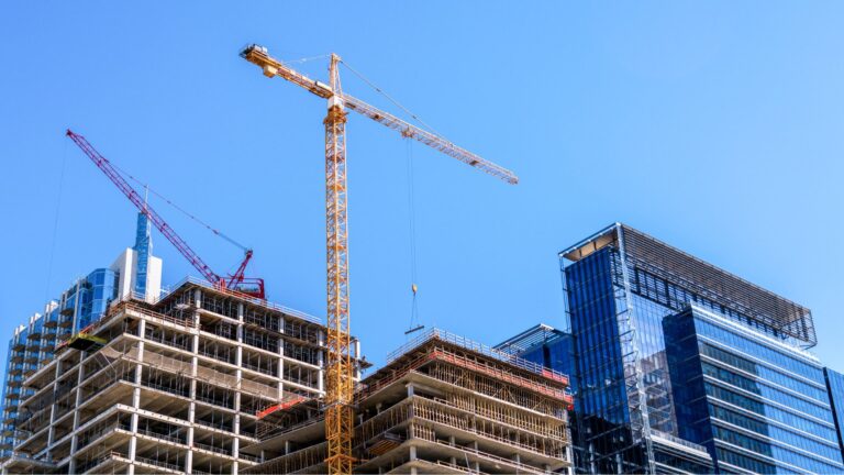 A high-rise building under development by construction companies in London featuring a large yellow tower crane against a clear blue sky.