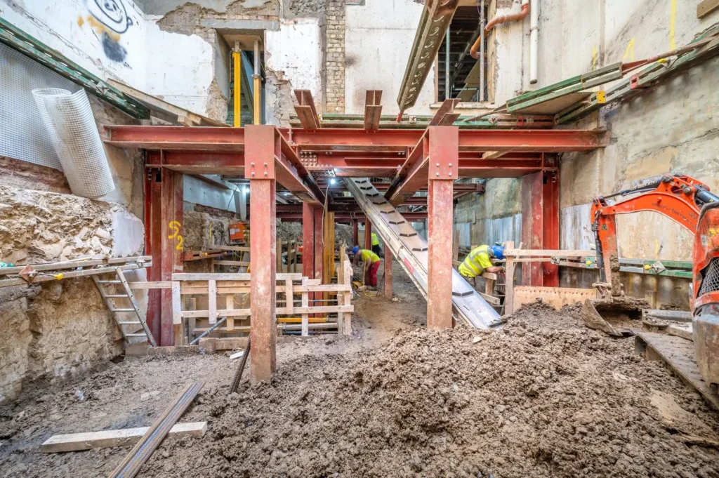 A deep basement excavation site in London featuring steel propping and conveyors, managed by specialist basement construction contractors in London.