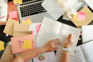 An overhead view of a busy student desk covered in notes and a laptop, illustrating the heavy workload requiring London assignment help for students in 2026.