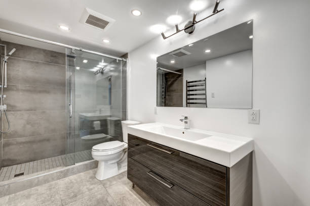 A modern, minimalist bathroom with a glass walk-in shower, grey tiles, and a floating dark wood vanity—illustrating high-end finishes that impact the total bathroom renovation cost UK.