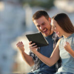 Excited couple checking tablet online content in a town