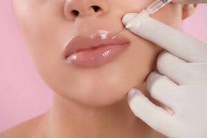 Young woman getting lips injection on pink background, closeup