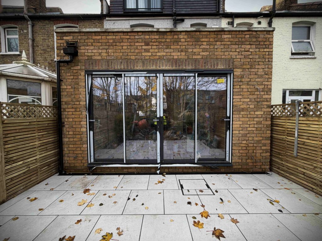 A newly completed rear brick house addition with large black-framed bifold glass doors and a light grey paved patio, perfect for home extension ideas in urban terraced properties.