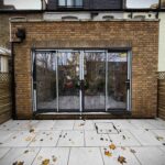 A newly completed rear brick house addition with large black-framed bifold glass doors and a light grey paved patio, perfect for home extension ideas in urban terraced properties.