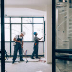 Two professional cleaners in safety gear and hard hats performing post-construction cleanup in a newly renovated London building, showcasing expert construction site cleaning services in UK.