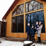 attractive-mother-with-her-kids-winter-day-stand-near-wooden-house-with-large-window_627829-230