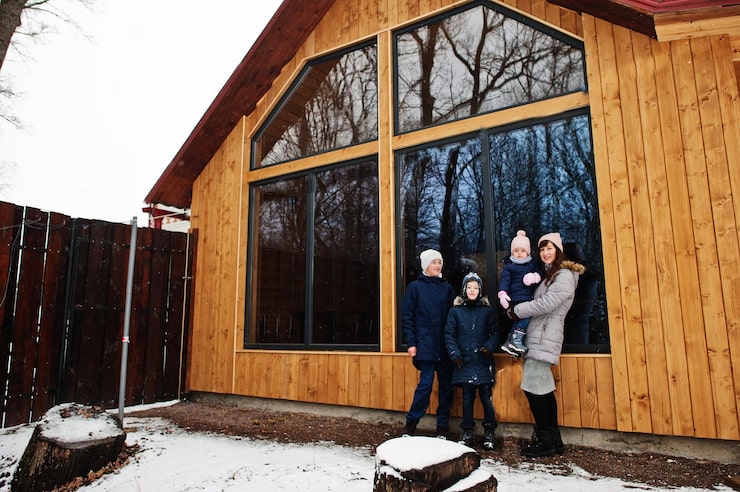 attractive-mother-with-her-kids-winter-day-stand-near-wooden-house-with-large-window_627829-230