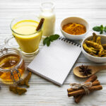 Golden turmeric latte in a glass, spices and recipe book over wh