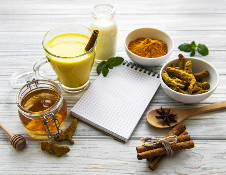 Golden turmeric latte in a glass, spices and recipe book over wh