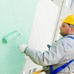 builder worker painting facade of high-rise building with roller