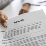 Businesswoman sitting at her desk in office giving resume paper to a person