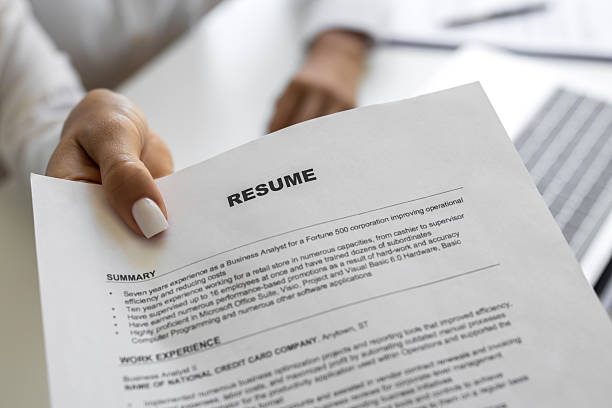 Businesswoman sitting at her desk in office giving resume paper to a person